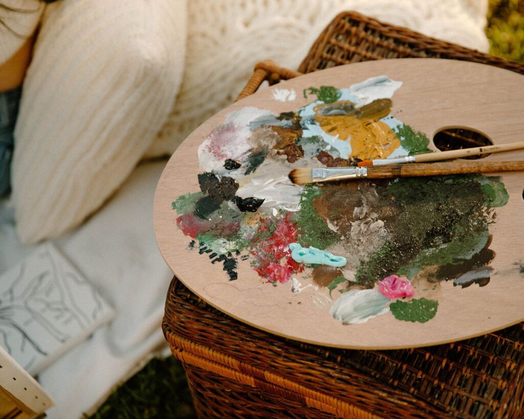 Paint palette and picnic basket in romantic park photoshoot.