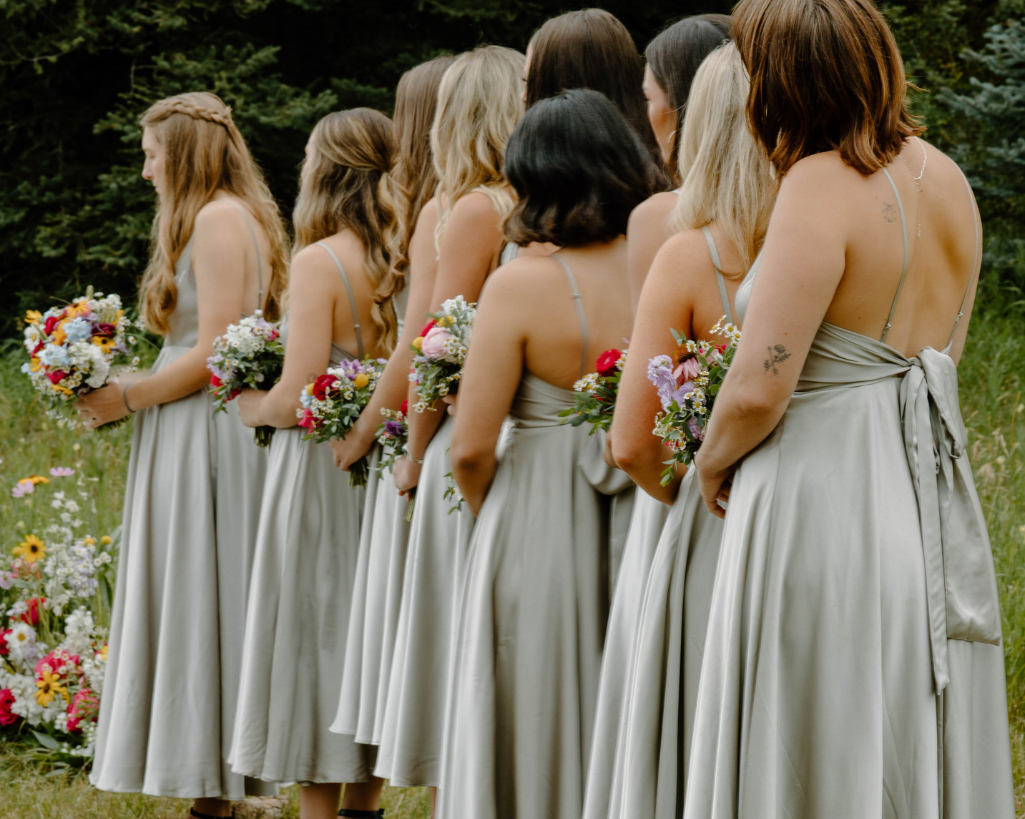 Bridesmaids in sage green dresses stand in a line by the bride's side.