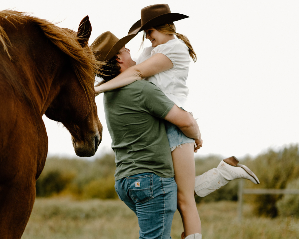 Fiance holds his soon to be bride in a lift around horses