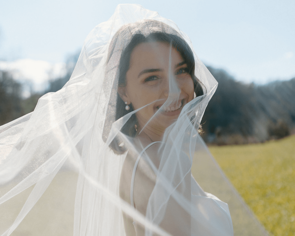 Bride smiles as sunlight hits the veil over her face.