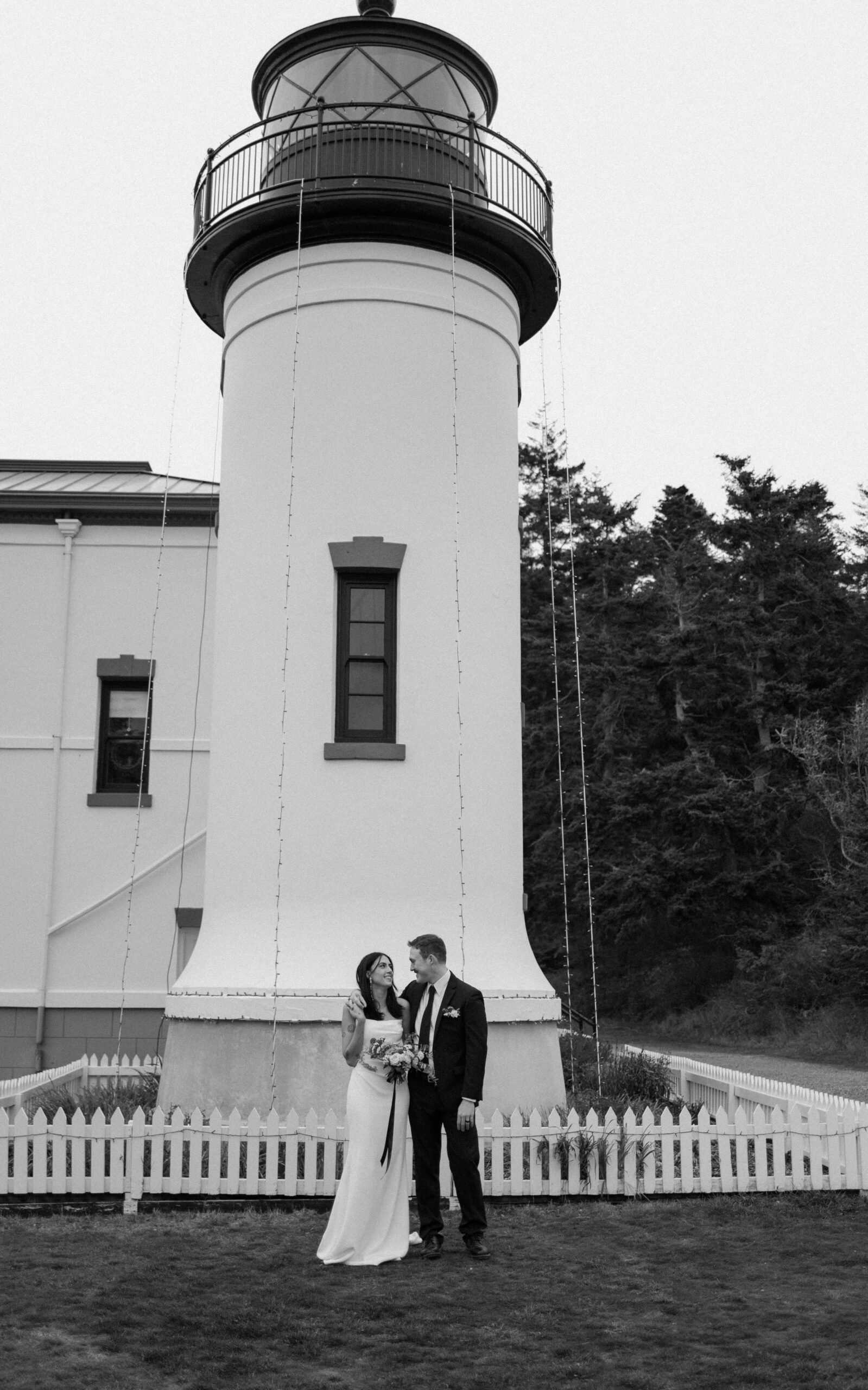 Bride and groom pose under lighthouse along Puget Sound in anti-bride elopement photos