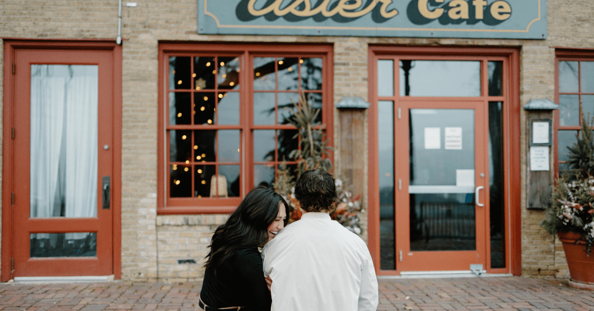 Woman leans her head on man's shoulder as they look at the Aster Cafe in Minneapolis engagement shoot