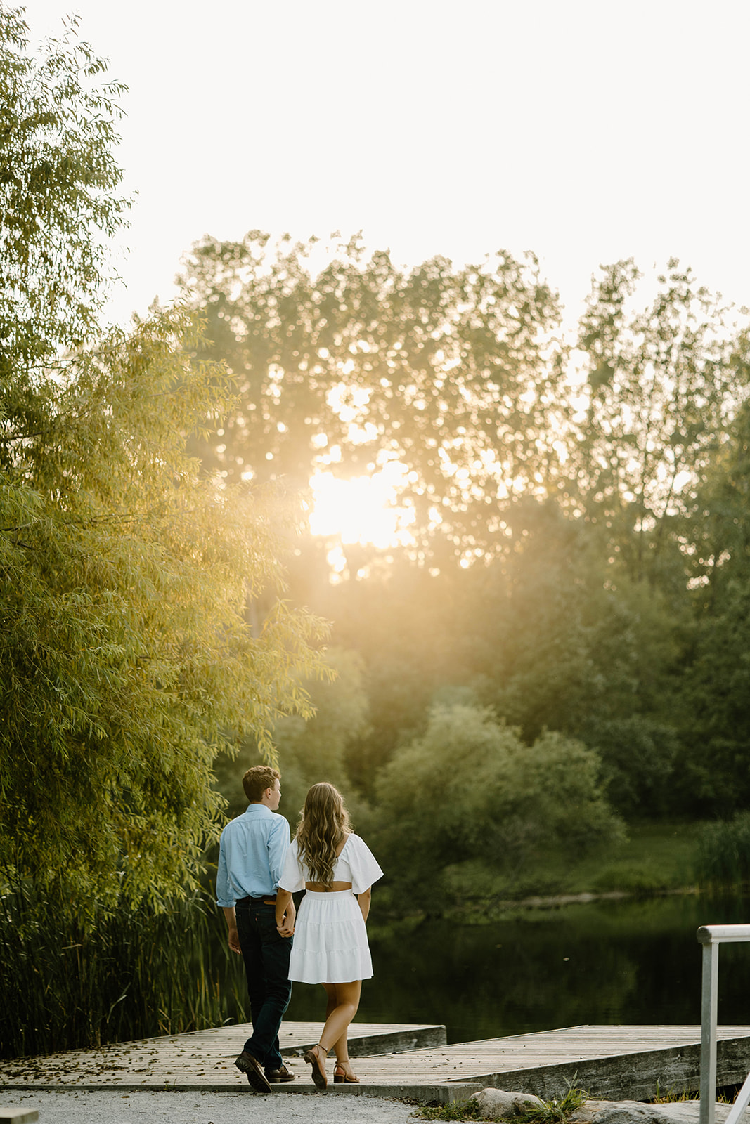 Man and woman wander down dock in Jester Park in golden hour engagement shoot.
