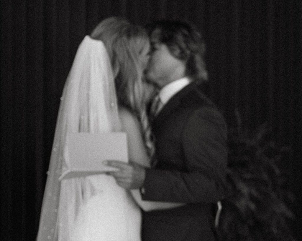 Bride and groom kiss in documentary-style black and white photo