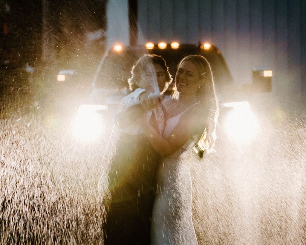 Newlyweds do champagne pop in front of truck headlights at the end of their wedding day