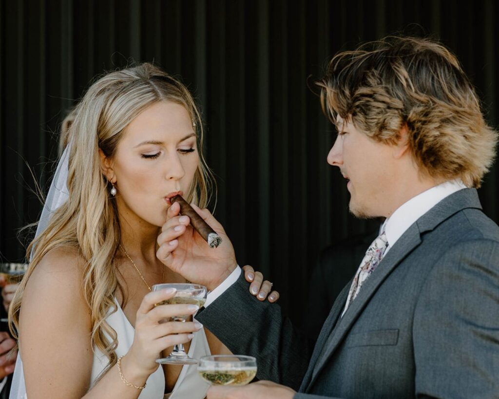 Groom holds cigar for bride while they champagne toast to their marriage