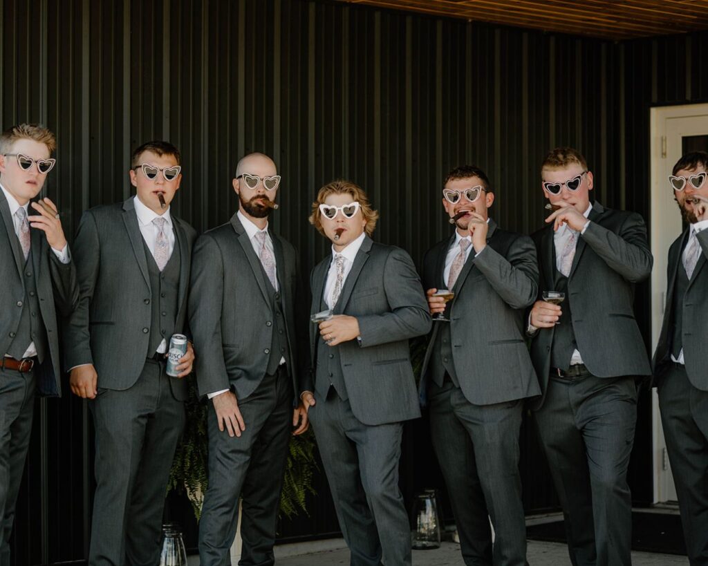 Groom and his groomsmen pose with heart-shaped sunglasses and cigars