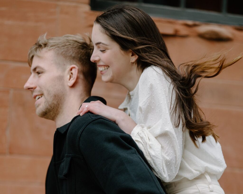 Woman rides on man's back piggyback style in playful engagement photoshoot.