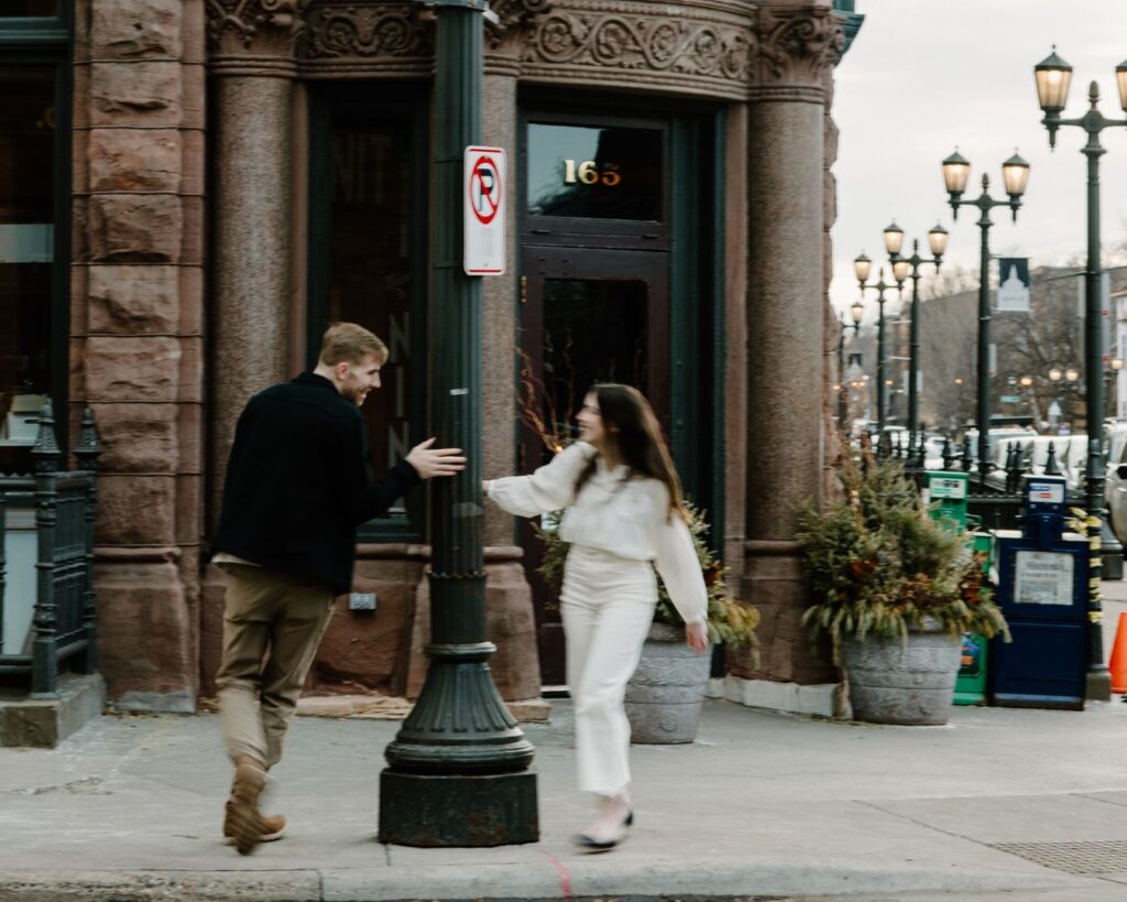 Blurry and playful photograph of engaged couple running around lamppost outside Nina's Coffee Cafe in Saint Paul, Minnesota.