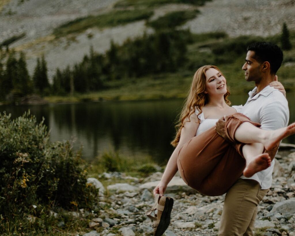 Boyfriend carries his girlfriend over rocky landscape surrounded by lush emerald green forest near Breckenridge, Colorado