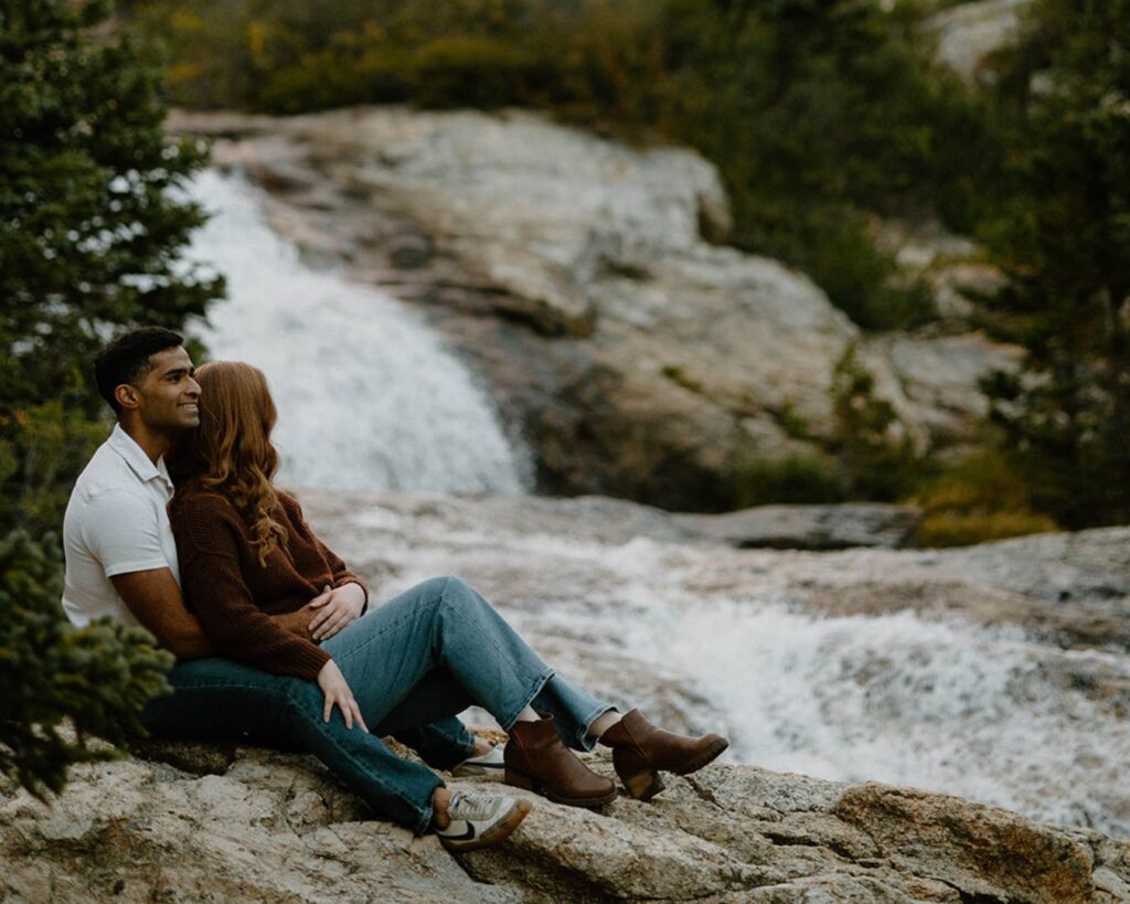 Couple sits on rock in loving embrace overlooking waterfall at Blue Lakes in Telluride, Colorado