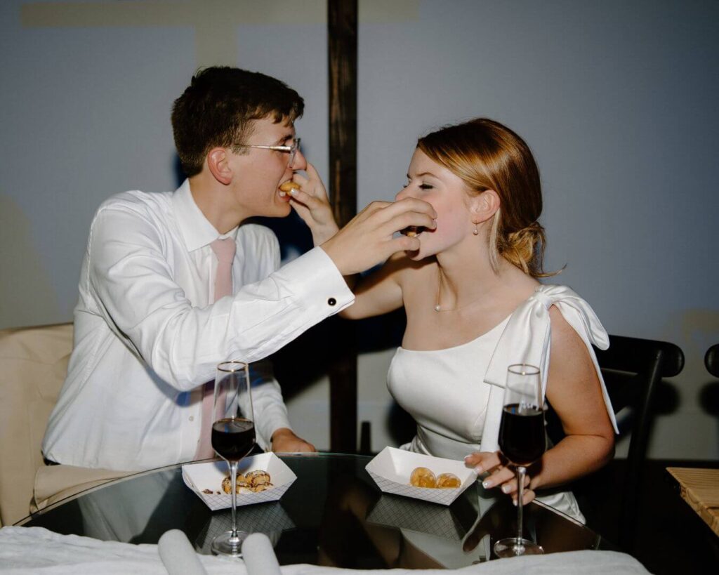 Bride and groom playfully feed each other donuts during reception, spring wedding ideas.