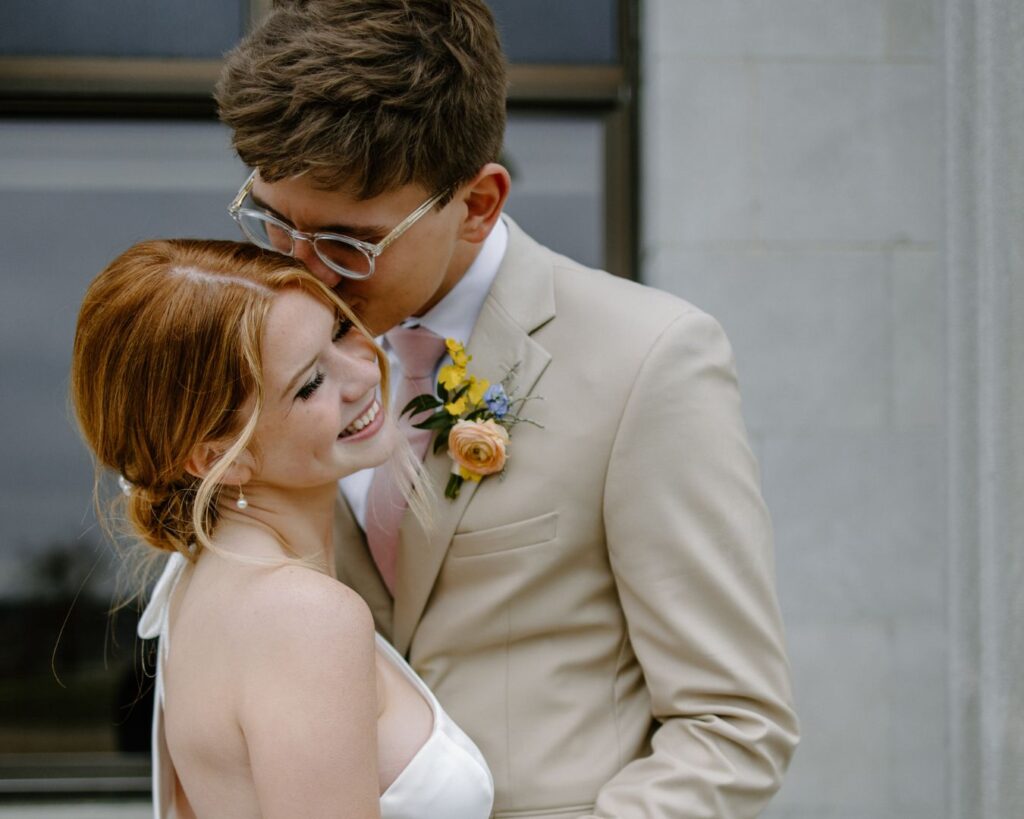 Groom lovingly kisses bride's cheek as she grins on her spring wedding day.