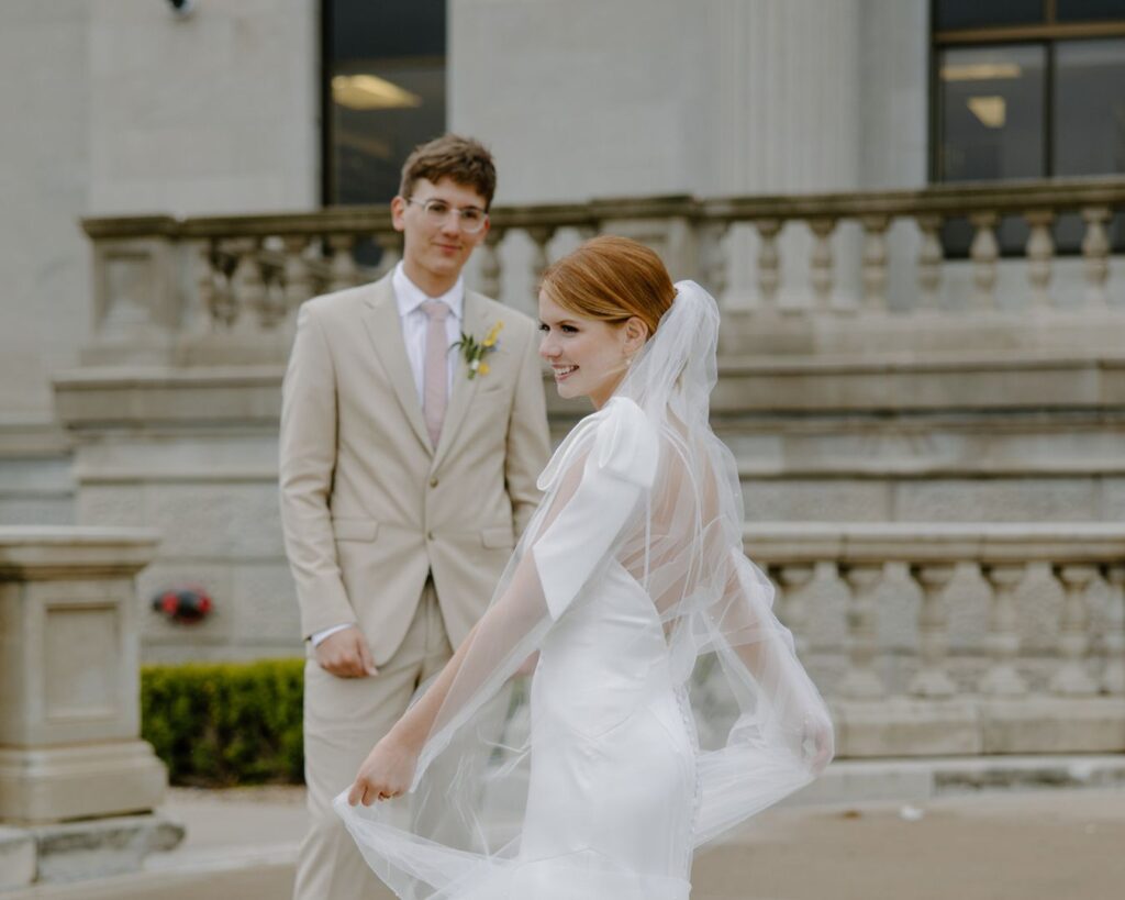 Bride twirls in asymmetrical wedding dress as groom looks on.