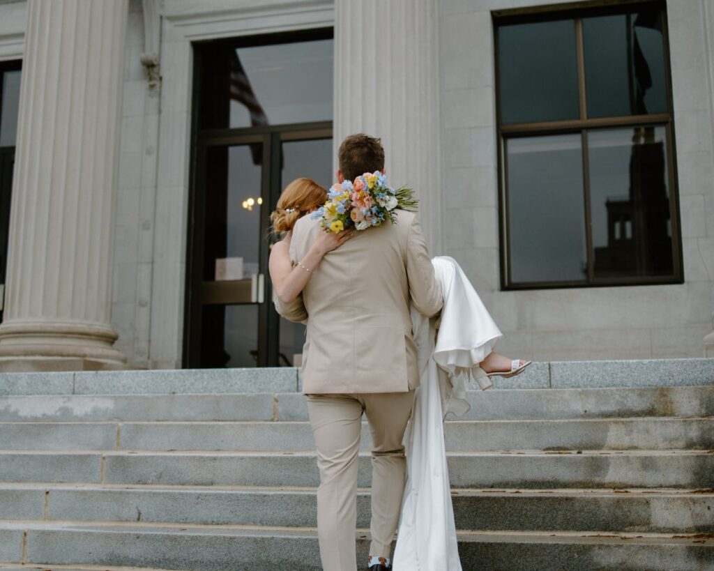 Spring wedding ideas, groom carries bride up steps of the courthouse.
