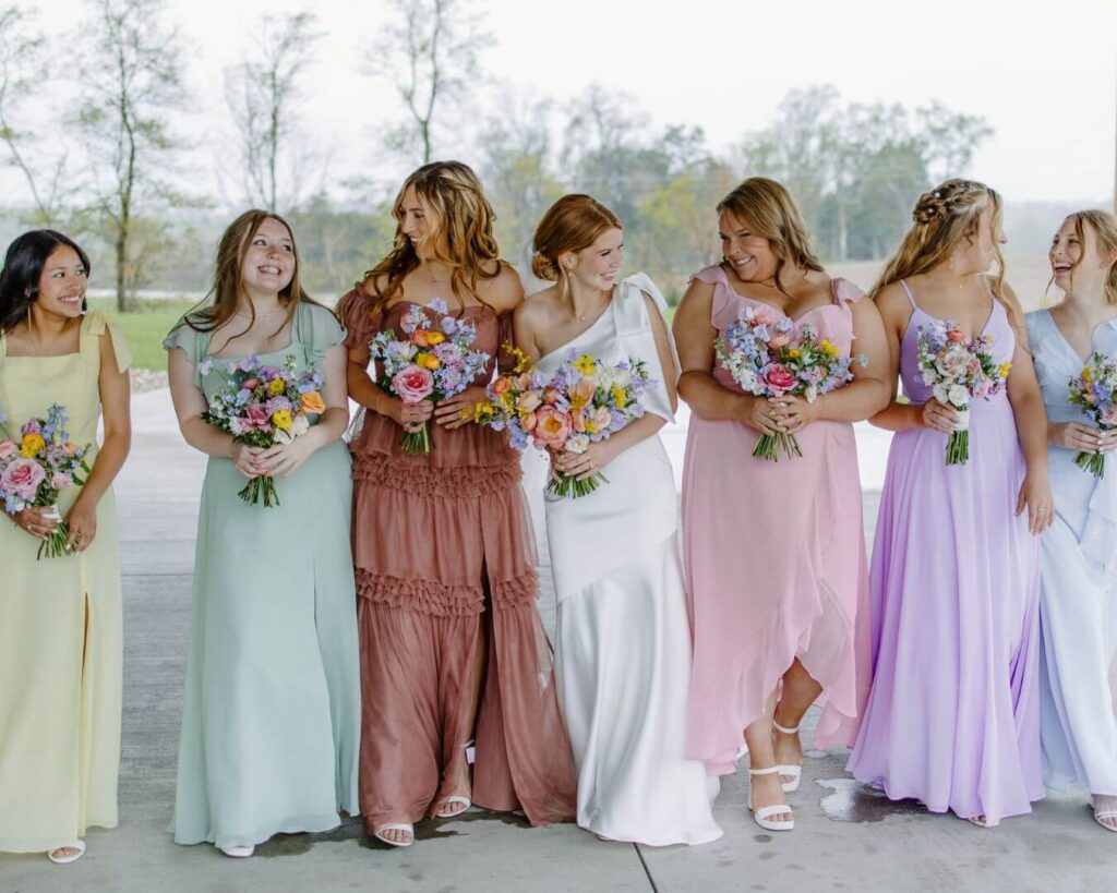 Bride and bridesmaids smile and laugh at each other in pastel bridesmaids dresses.