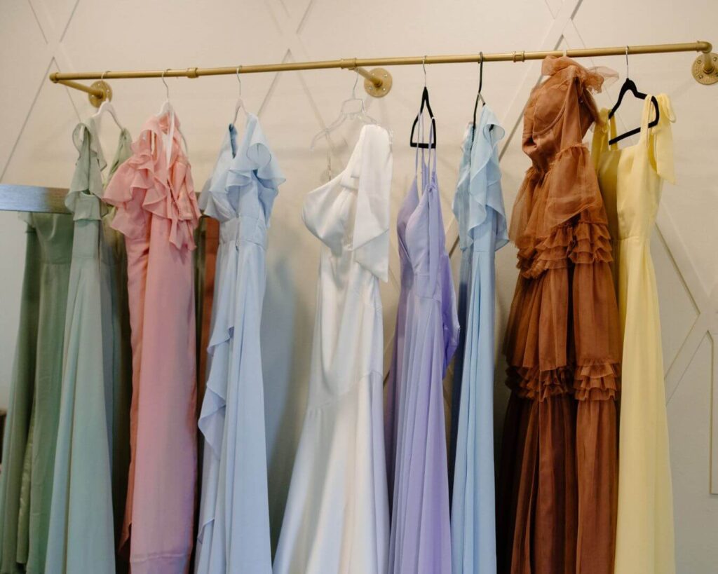 Pastel bridesmaids dresses hang alongside bride's asymmetrical wedding gown. 