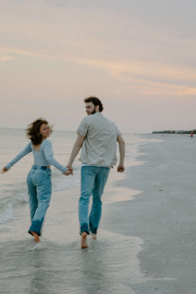 Couples runs off into the sunset on Sanibel Island beach during adventure engagement photoshoot.