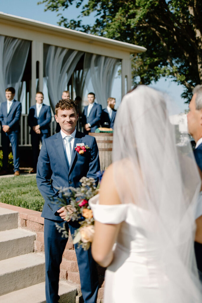 Groom smiles at bride as she walks down the aisle towards him