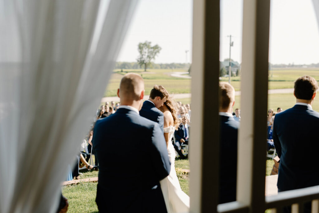 Documentary-style photographer sneeks photo of bride and groom exchanging vows through the curtains