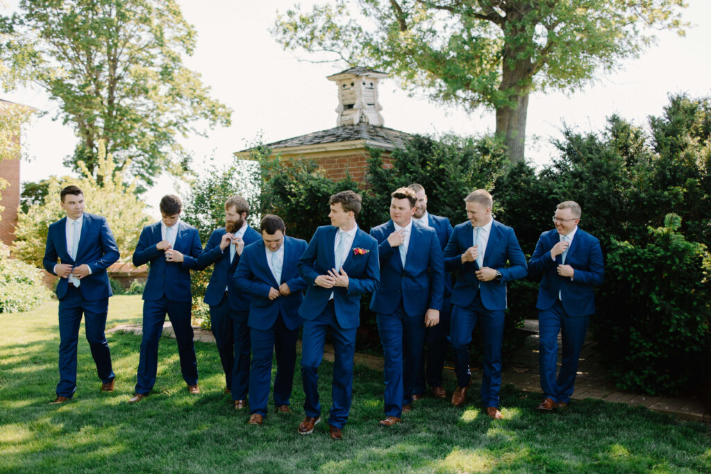 Groomsmen wear rich blue suits and walk in the grass