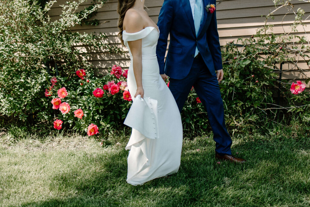 Bride and groom walk among bright pink peonies