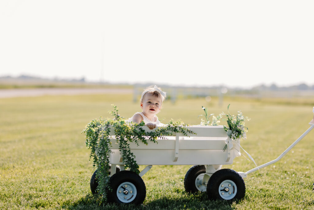 Flower girl comes down the aisle in eucalyptus adorned white wagon