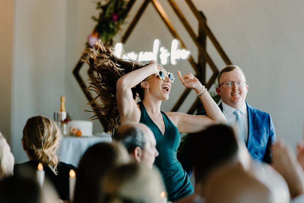 Documentary-style photographer captures bridesmaid dancing with flower sunglasses on.