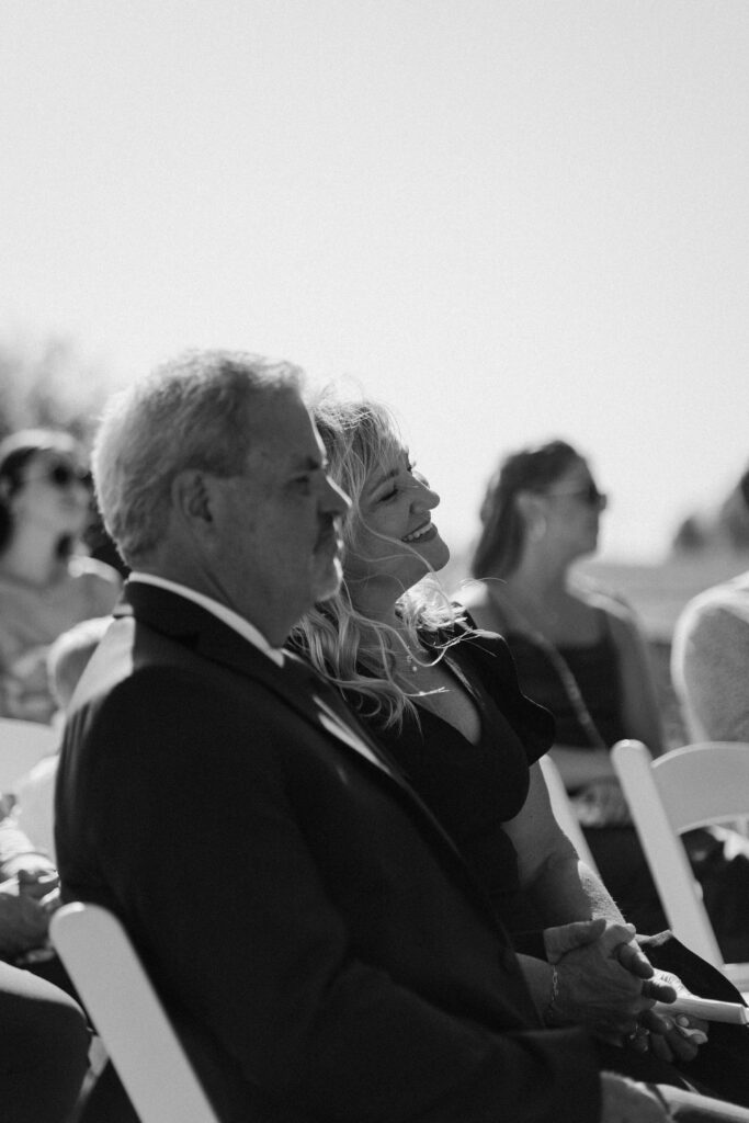 Parents of the bride smile as the bride and groom exchange their vows in documentary-style photography wedding