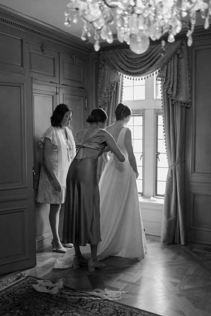 Maid of honor and mother of the bride button up bride's gown with chandelier in the foreground of the photo