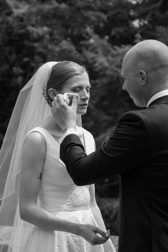 Groom wipes a tear from bride's eye as she reads her vows to him