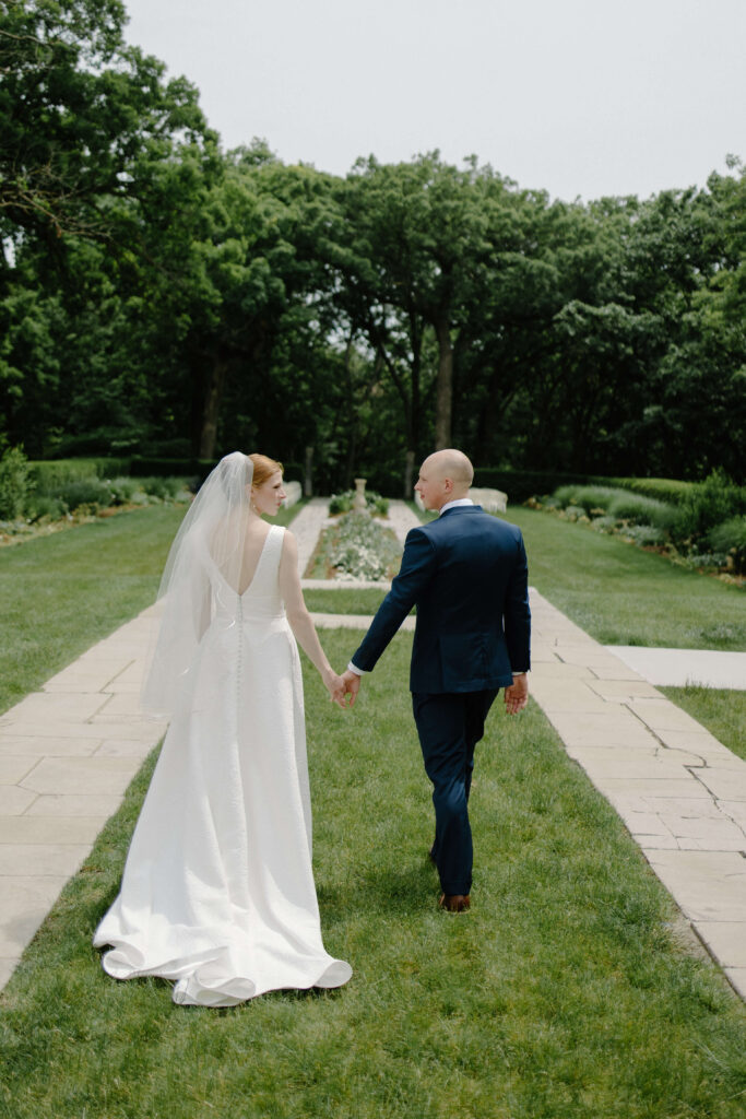 Bride and groom walk through gardens at their garden wedding