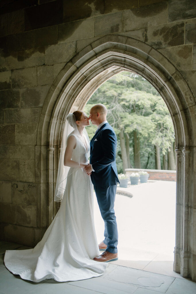 Groom steals a kiss in the archway of historic garden wedding venue