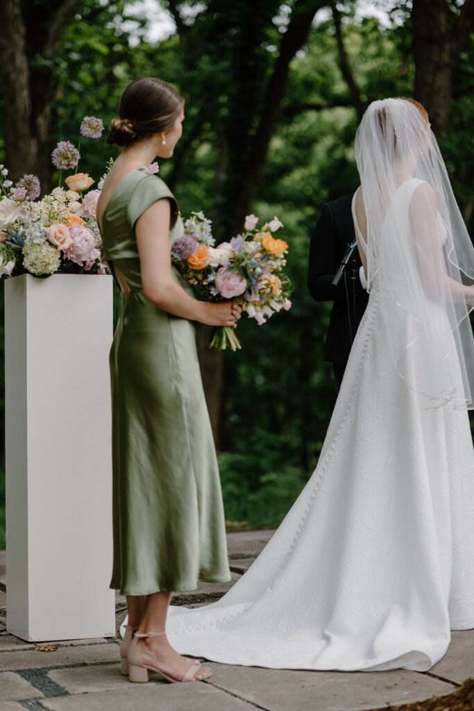 Maid of honor holds bride's bouquet as the newlyweds exchange their vows in garden wedding ceremony