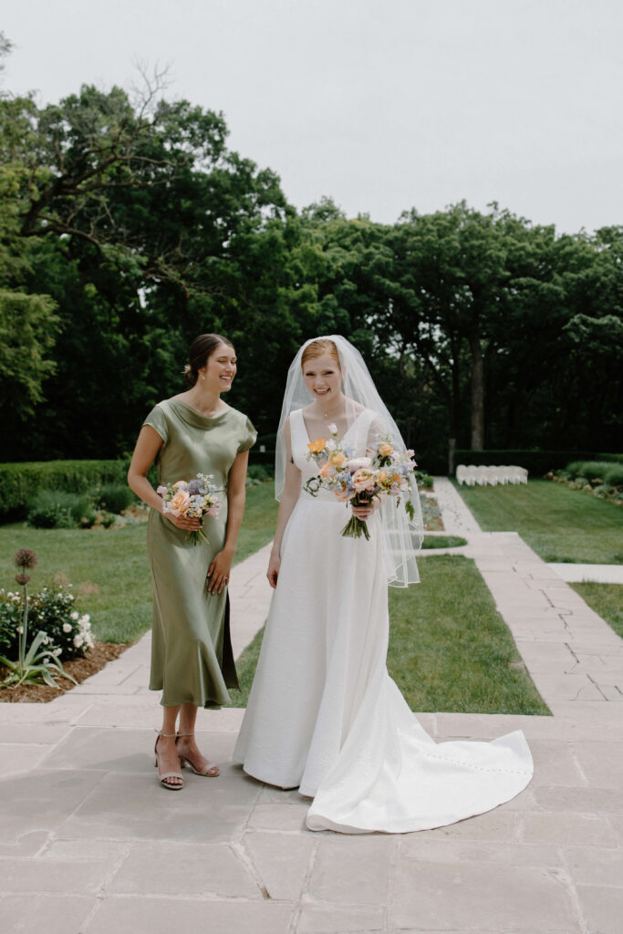 Maid of honor and bride laugh together in garden wedding