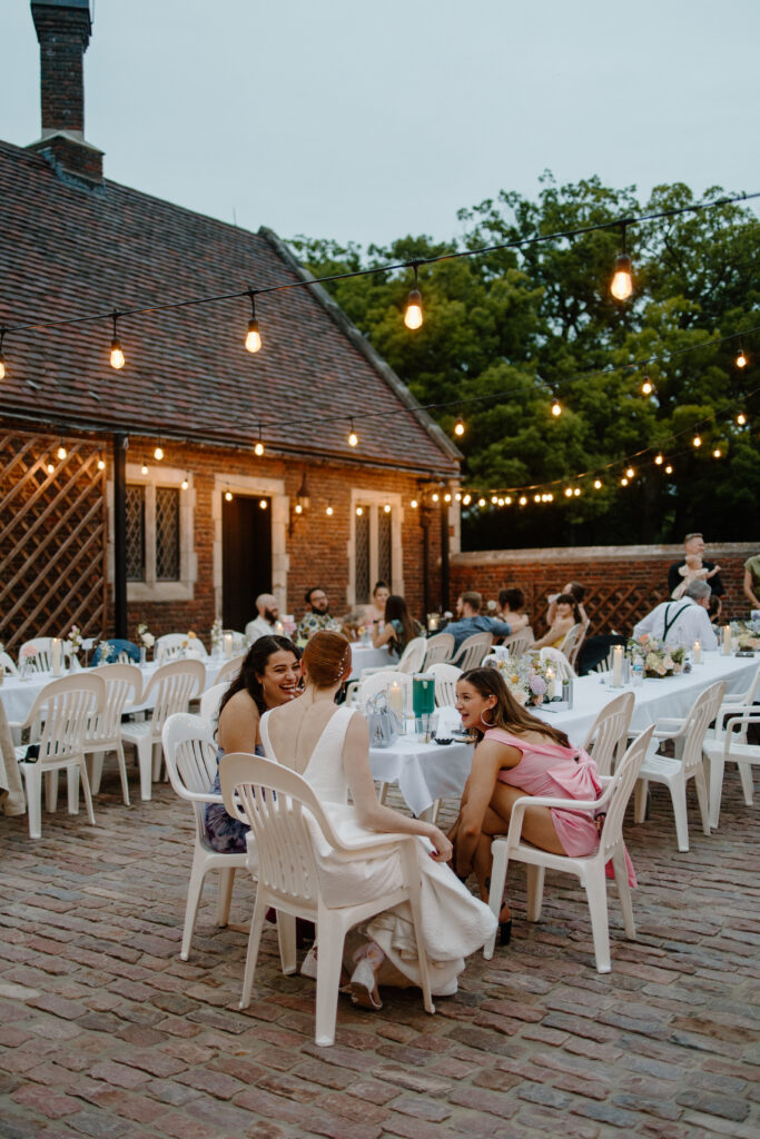 Bride and friends sit under the string lights as night falls at garden wedding