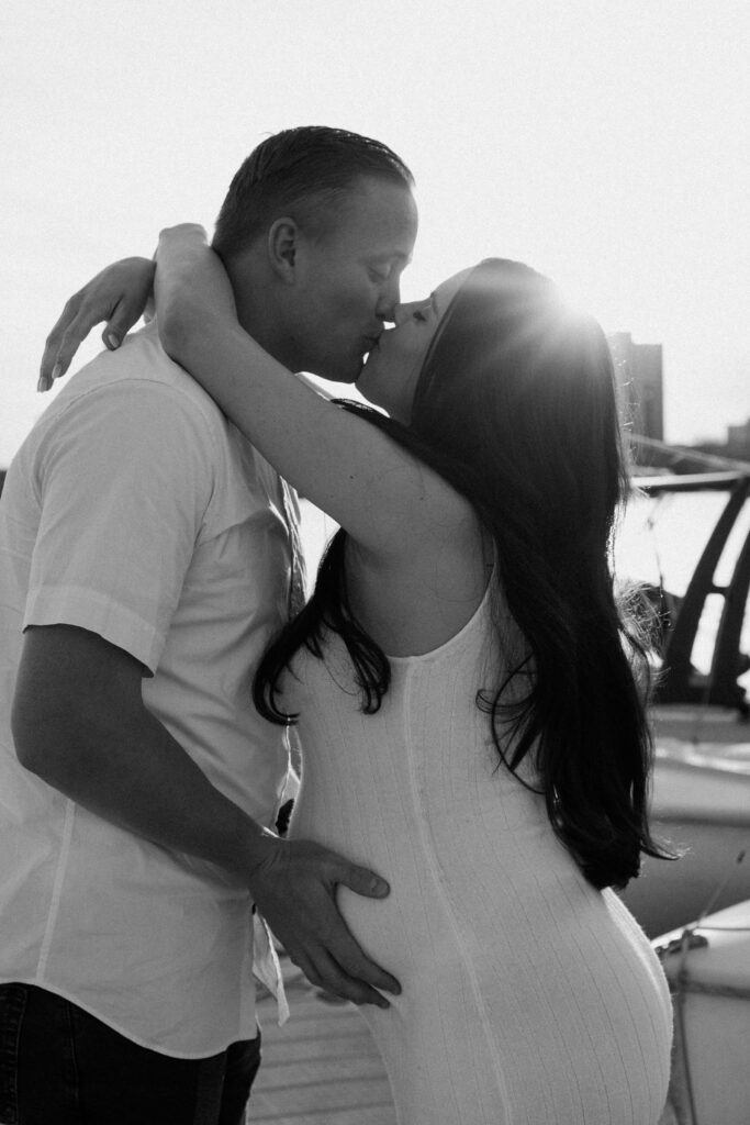 Man holds woman's pregnant belly as they kiss on the shore of Bde Mka Ska. 